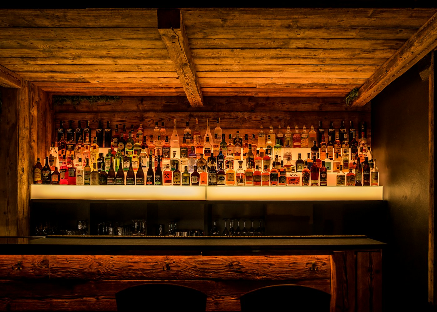 A warm, backlit back-bar wall lined with rows of bottles